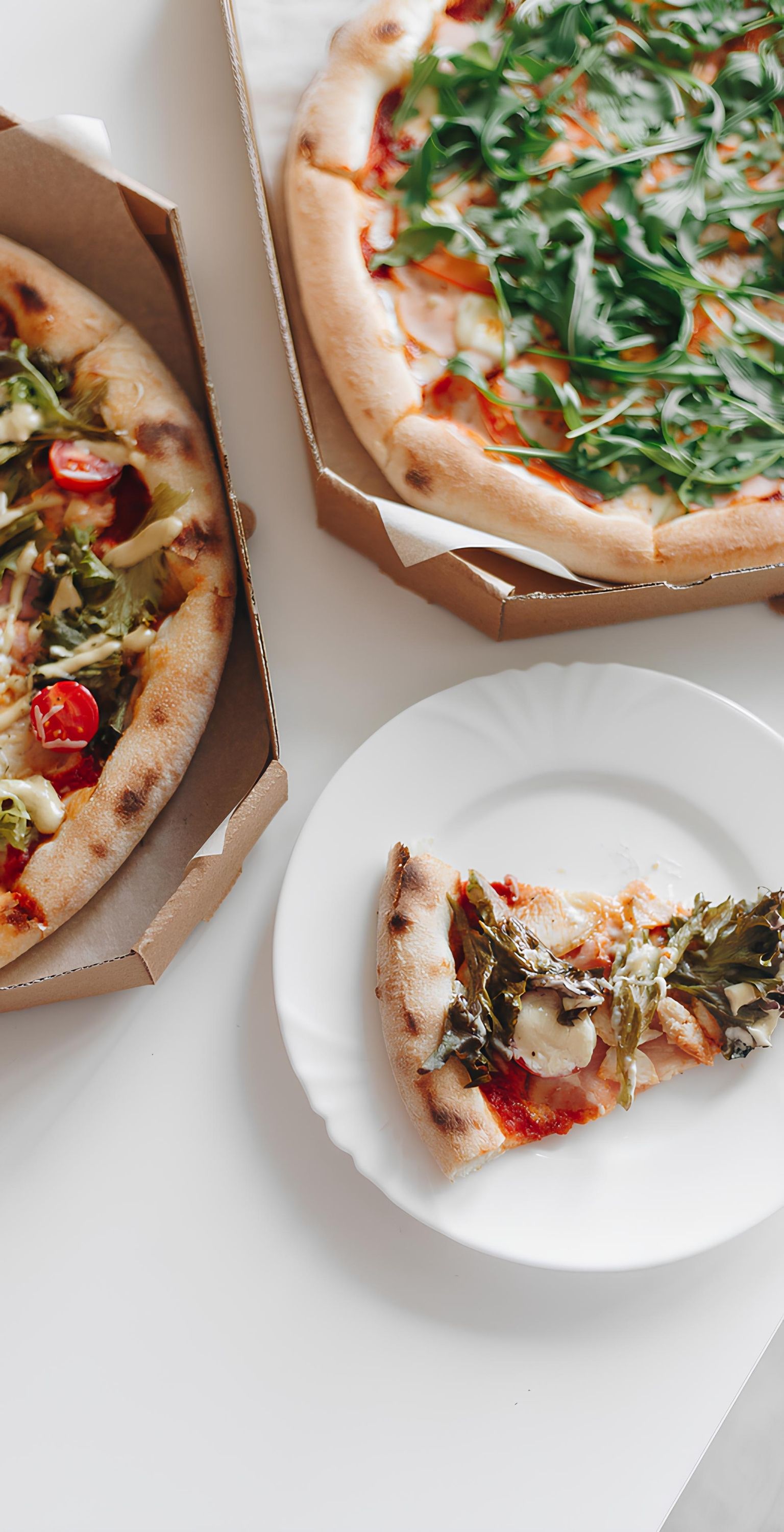Eine Pizza mit Rucola und Tomaten in einer Schachtel und ein Stück auf einem weißen Teller